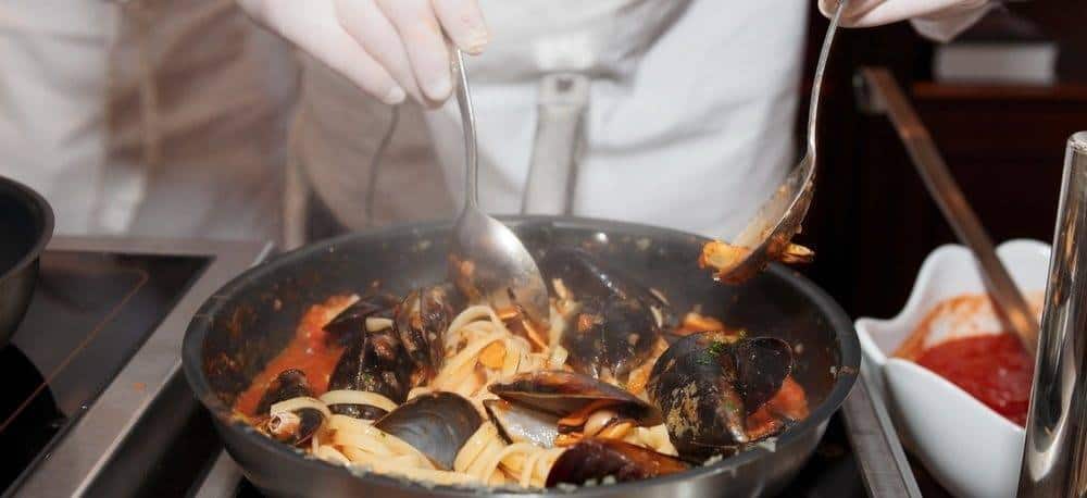 A pan being used for cooking a pasta and clam based dish in a restaurant.