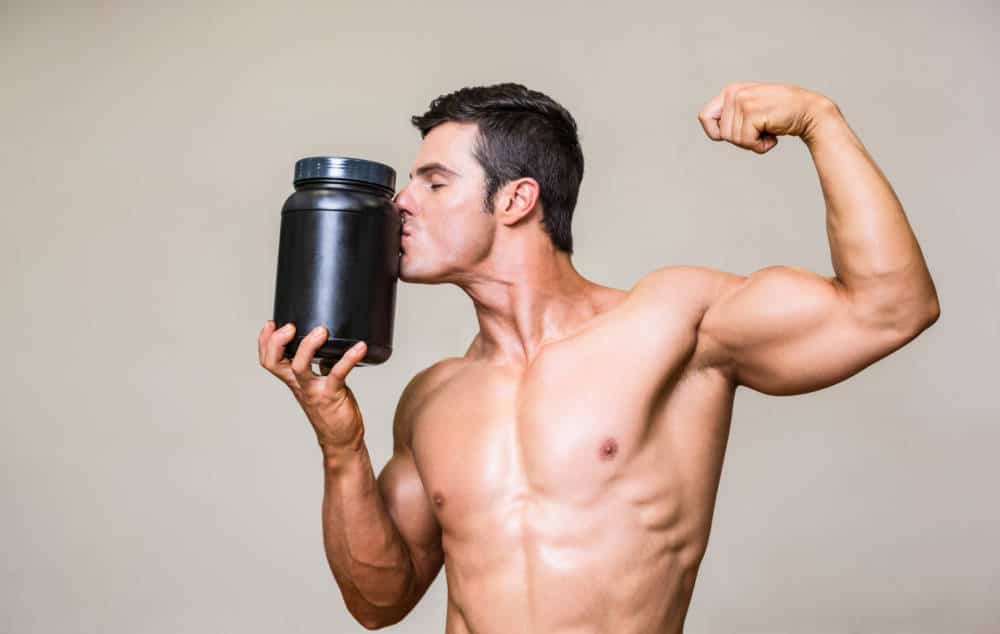 A muscular man kissing a large protein shake bottle.