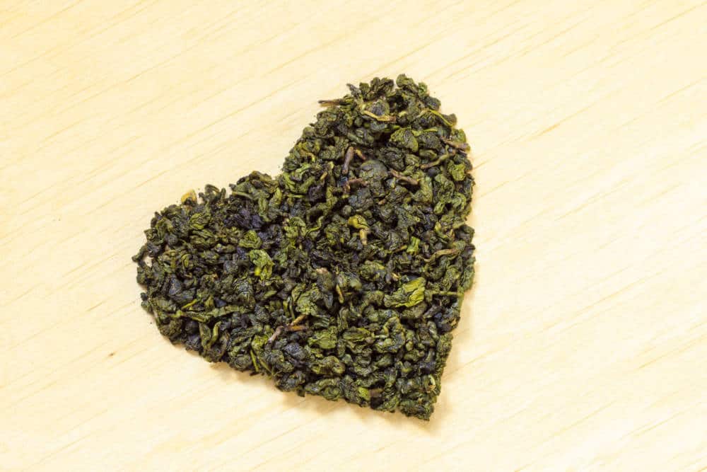Green tea leaves heart shaped on wooden surface
